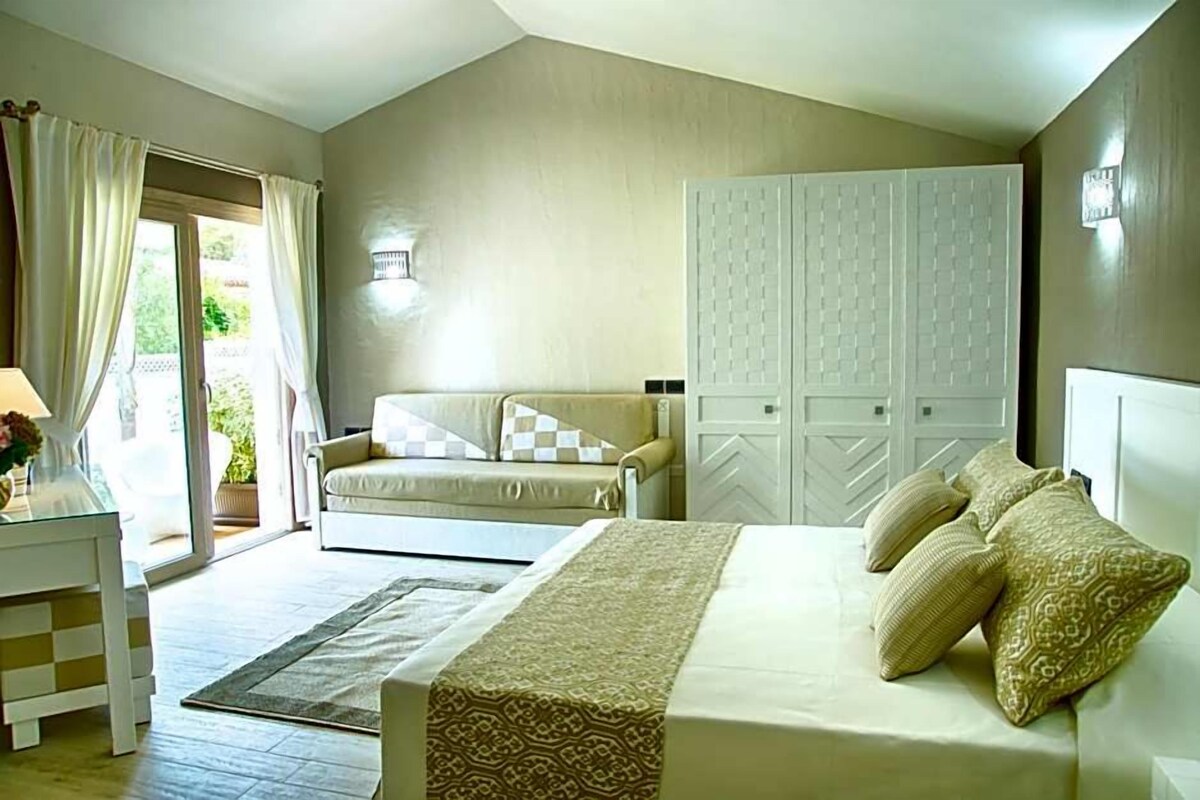 A bedroom with a bed, a sofa, a wardrobe, and a window with curtains.