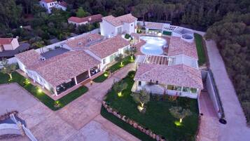 Un edificio grande de varios pisos con piscina, rodeado de exuberante vegetación y otras edificaciones residenciales.
