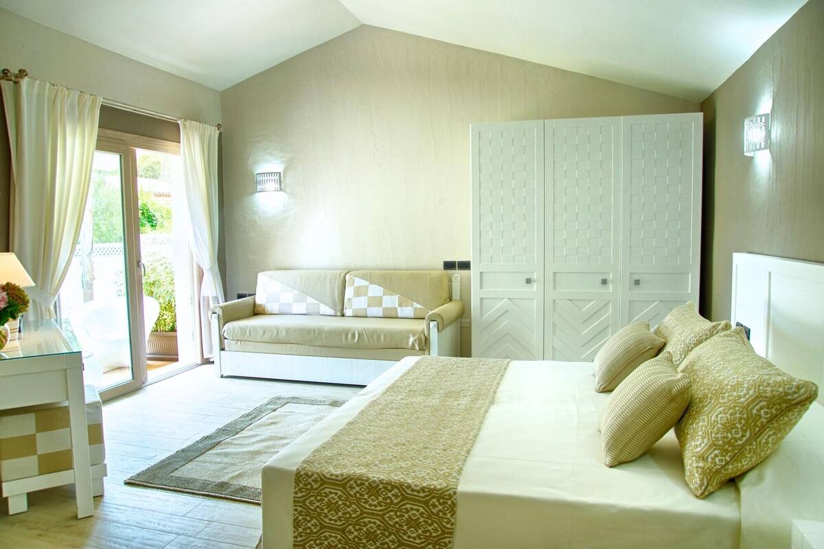 A bedroom with a bed, a sofa, a wardrobe, and a desk with a lamp.