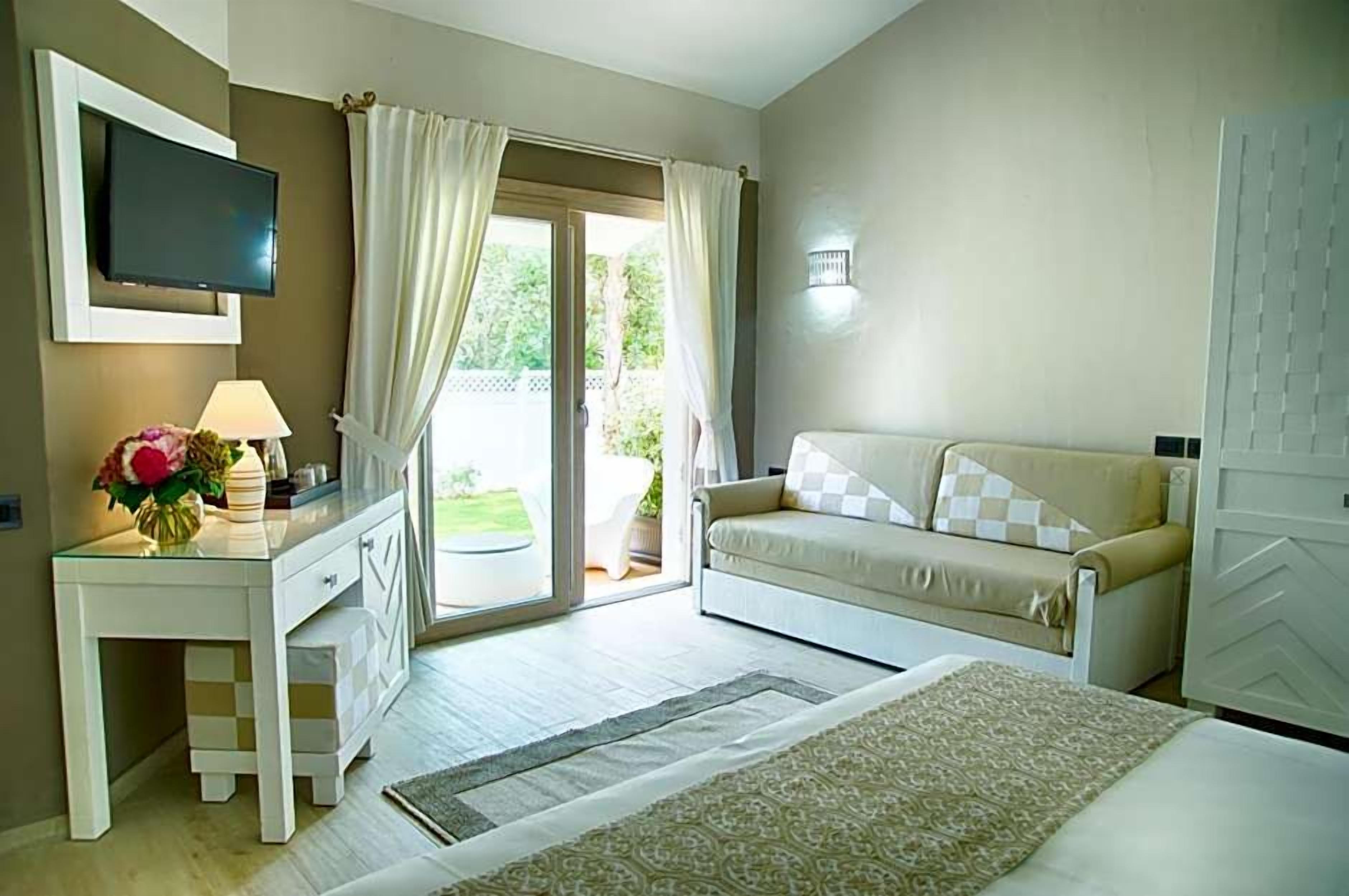 Un dormitorio con cama, sofá, televisor, escritorio y ventana con cortinas.