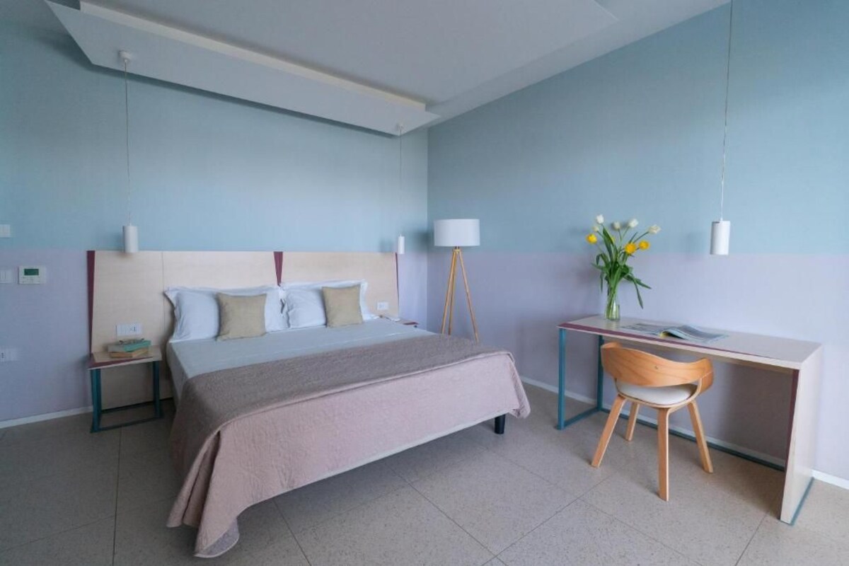 Ein modernes Hotelzimmer mit Bett, Nachttisch, Schreibtisch, Stuhl und einer Vase mit Blumen.