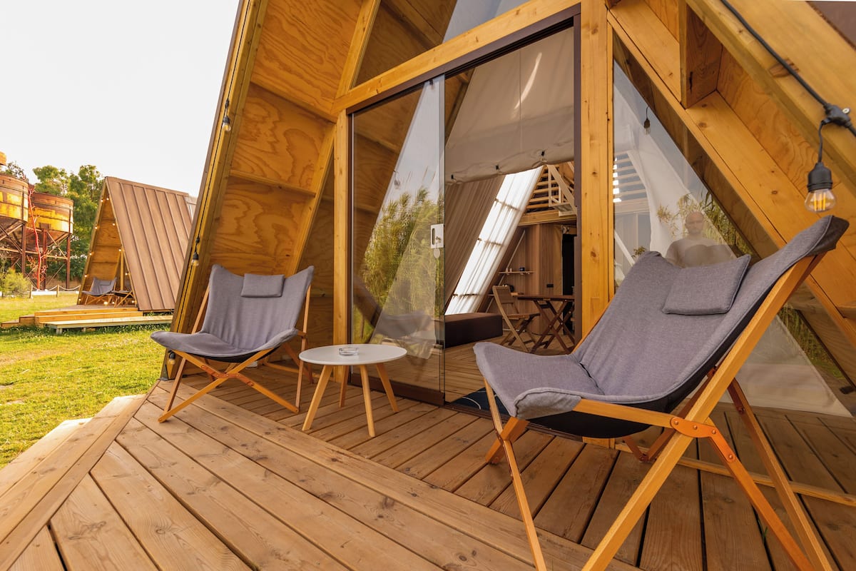 Een A-frame houten constructie met twee ligstoelen en een kleine tafel op het terras.