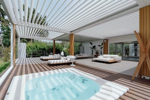 Un espace de détente extérieur moderne, doté d’un jacuzzi, d’une terrasse en bois et de canapés blancs.