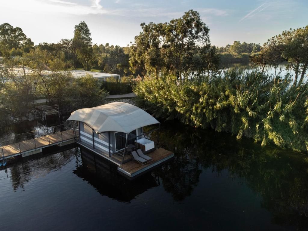 Una casa flotante con terraza techada y sillas de descanso, rodeada de agua y árboles.