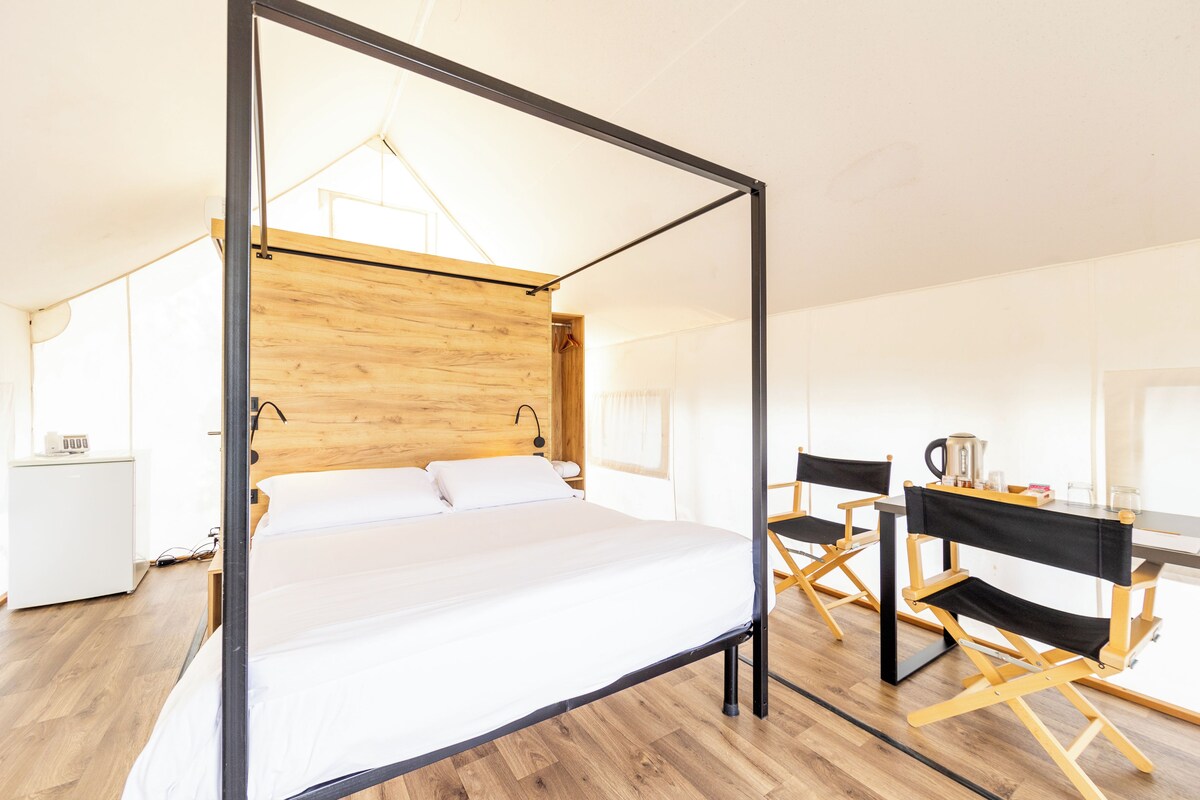 Ein modernes Hotelzimmer mit einem Bett mit Holz-Kopfteil, einem Schreibtisch mit Stuhl und einer kleinen Küchenzeile.