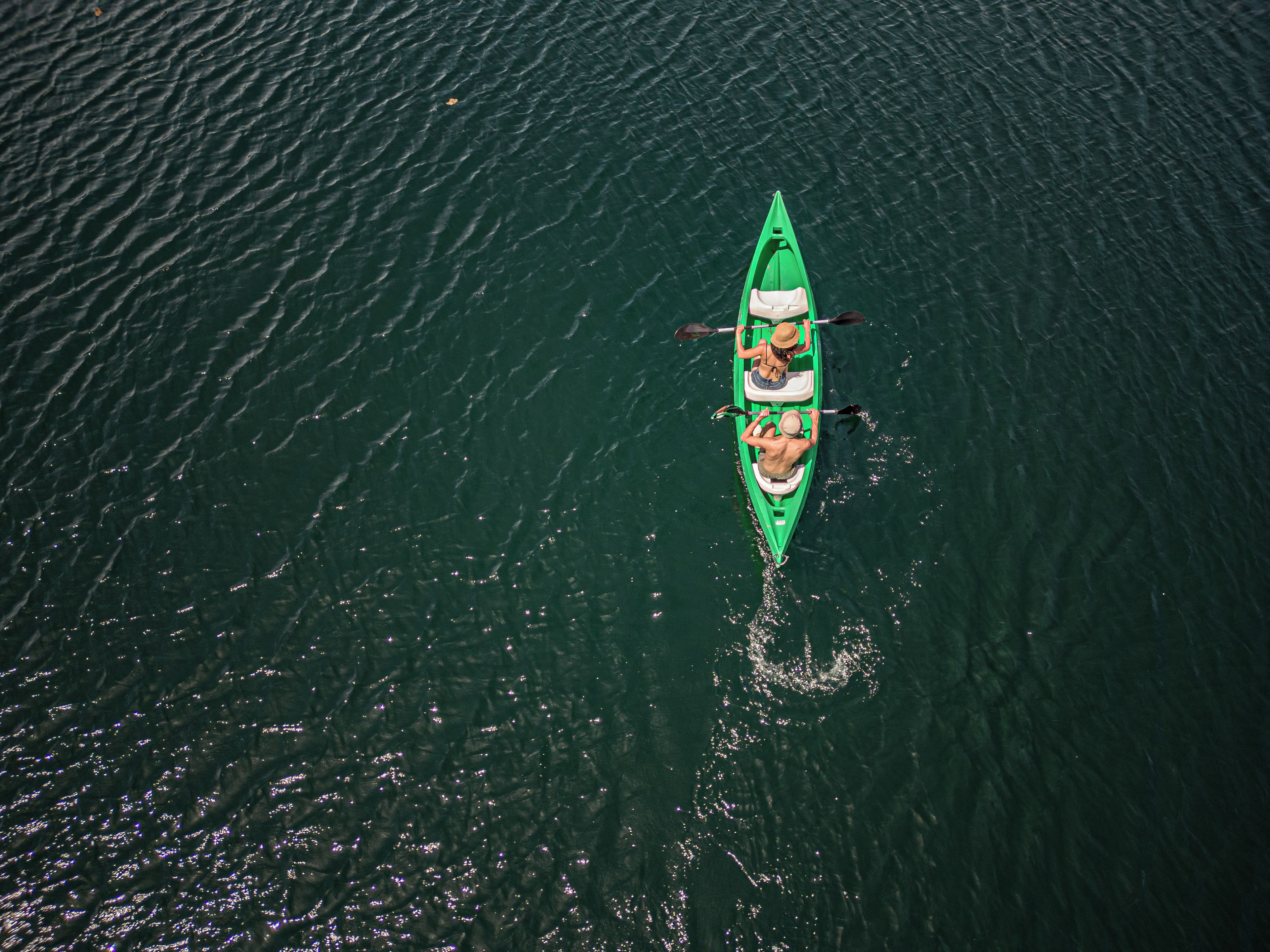 A green kayak with two paddlers on a calm body of water.
