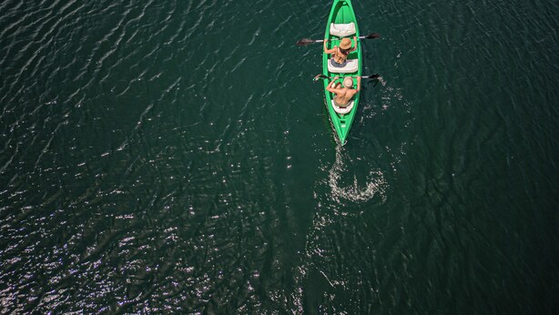 Un kayak vert avec deux personnes qui pagayent sur une étendue d’eau calme.