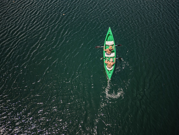 Un kayak vert avec deux personnes qui pagayent sur une étendue d’eau calme.