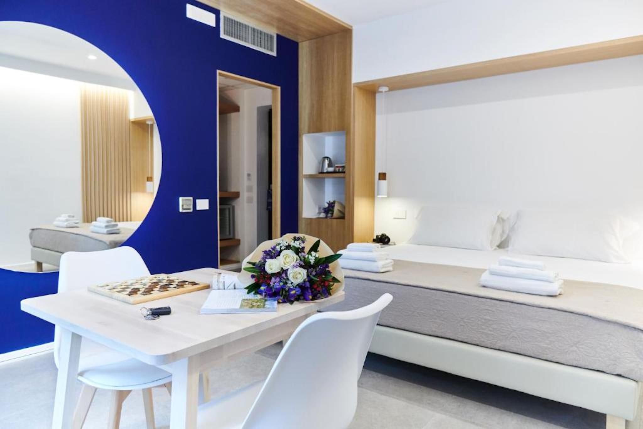 Una habitación de hotel moderna con un escritorio blanco, un tablero de ajedrez, un ramo de flores y una cama bien hecha.