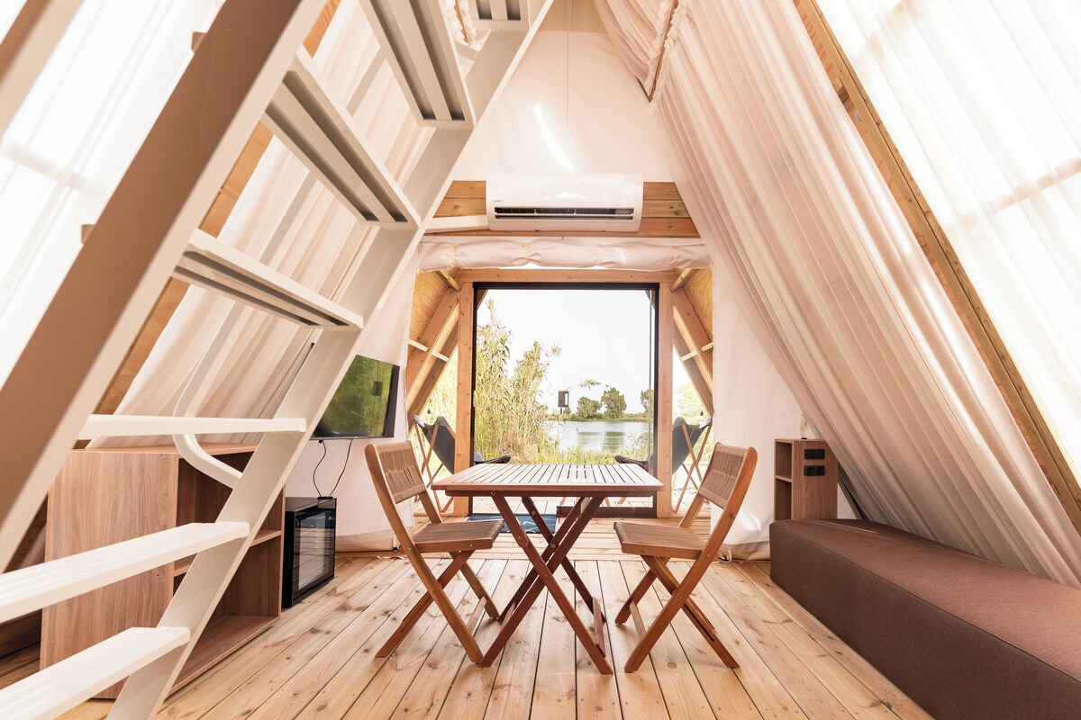 Acogedor dormitorio en el ático con una mesa de madera y sillas, un televisor pequeño y una ventana con vistas a zonas verdes.