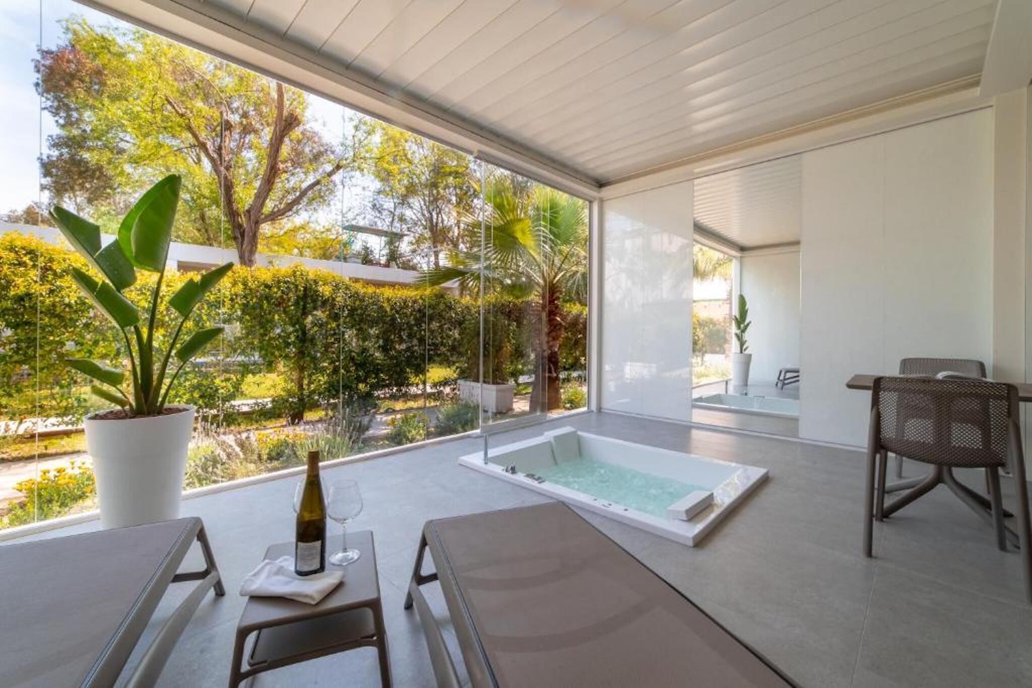 Un espace spa moderne doté d’un jacuzzi, de sièges et offrant une vue sur un jardin.