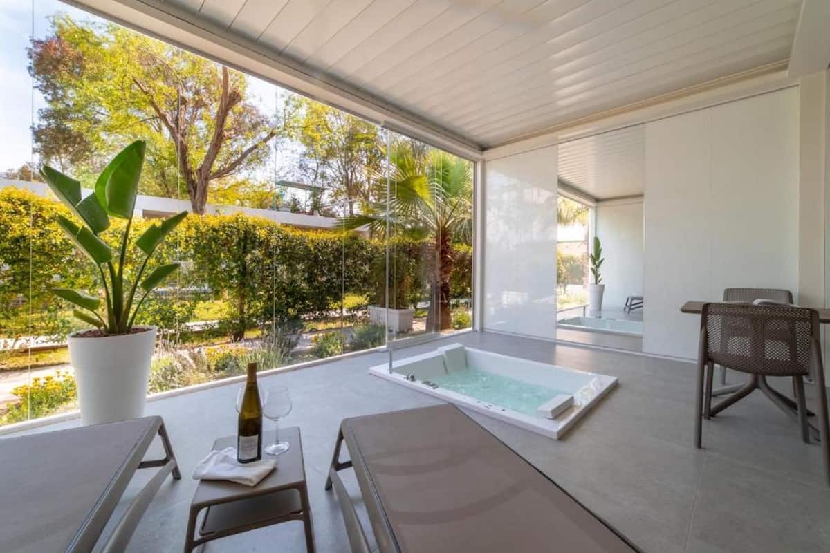 Een moderne spa-ruimte met een groot raam, een jacuzzi en een zithoek met een tafel en stoelen.