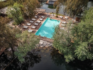 Eine Vogelperspektive zeigt einen Urlaubsort mit einem rechteckigen Pool, der von Liegestühlen und einer Holzterrasse umgeben ist.