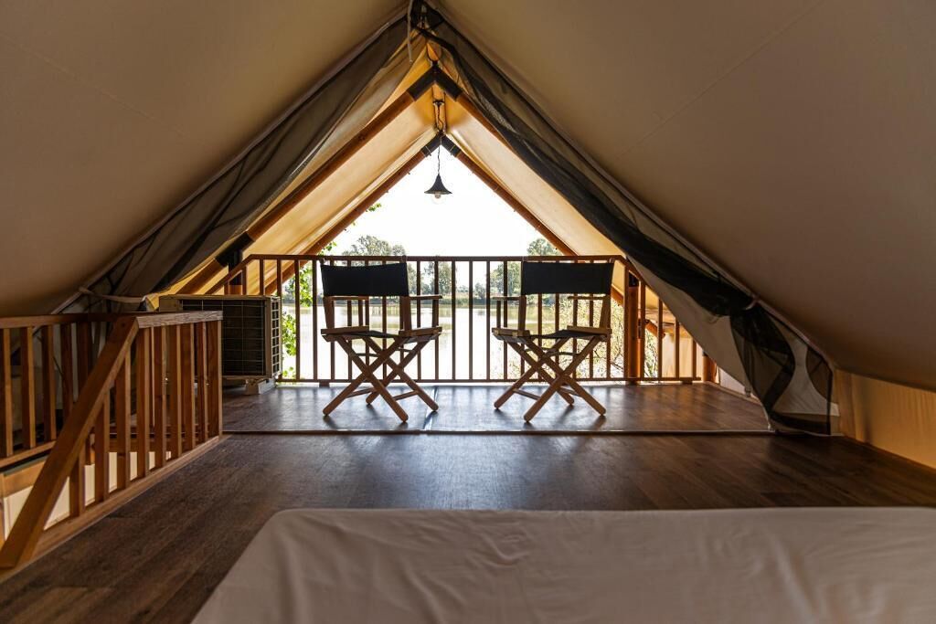 Une chambre confortable située dans les combles, avec un plancher en bois, un lit et un balcon agrémenté de deux chaises en bois.