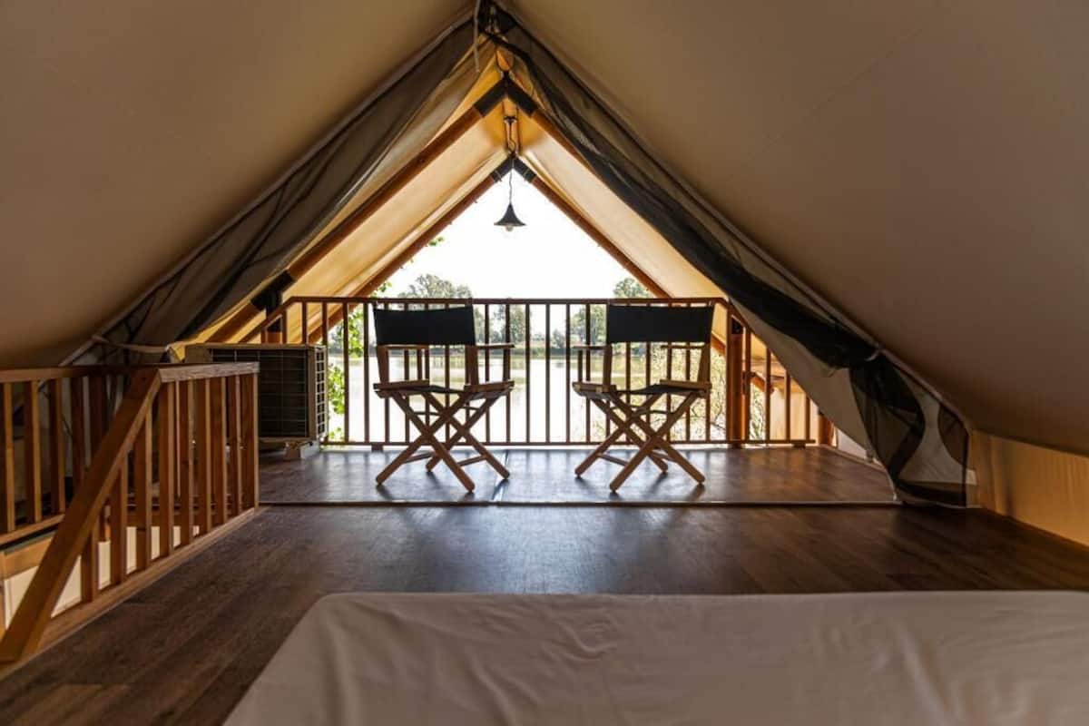 Een gezellig zolderkamer met houten vloer, een bed en een balkon met twee houten stoelen.