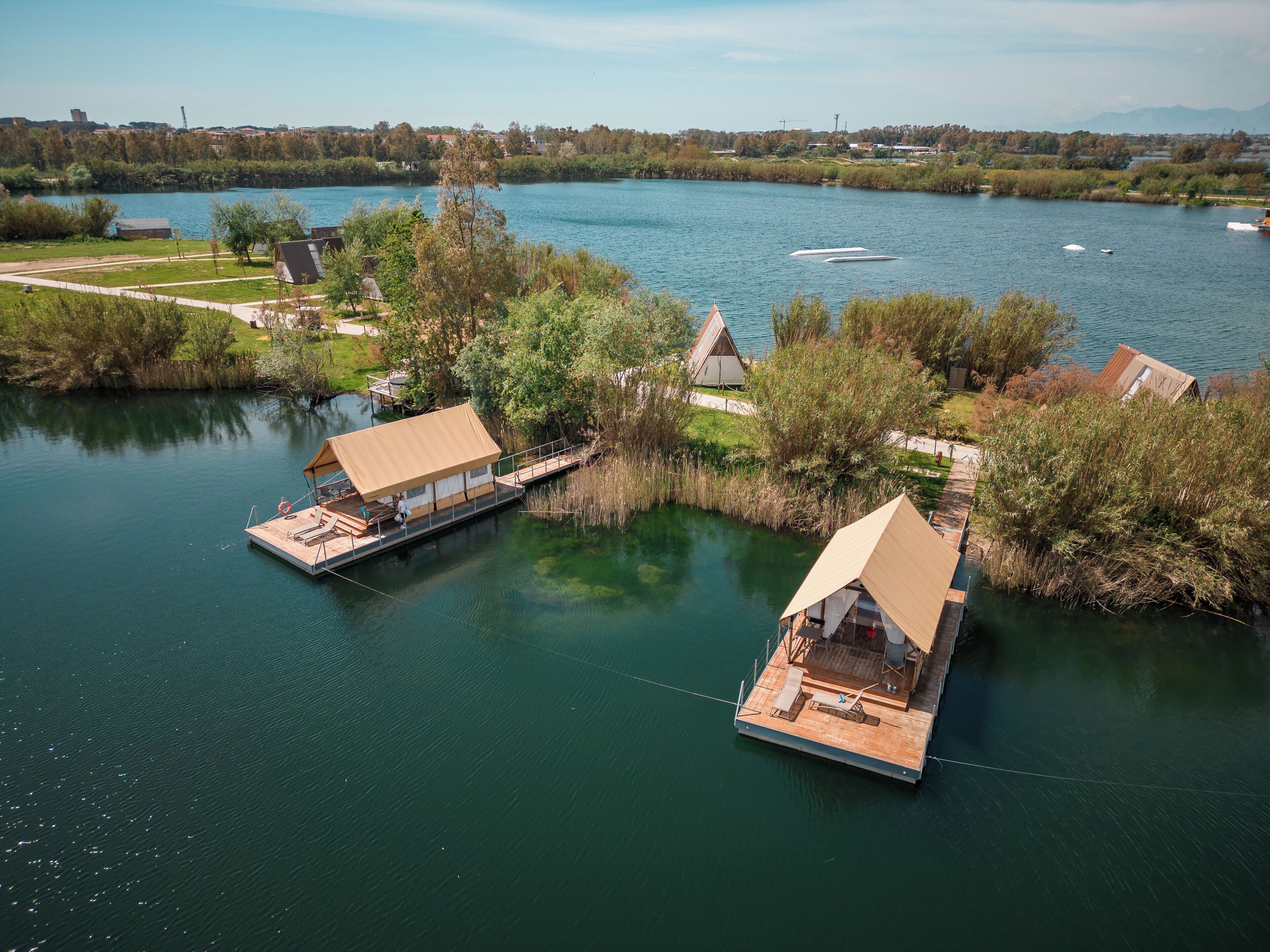 Deux structures flottantes, dotées de toits et reliées par un pont, sur une rivière paisible.