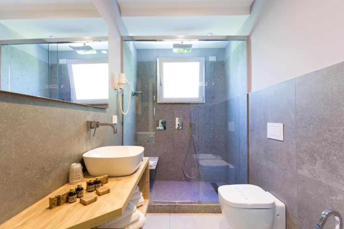 Un baño moderno con un lavamanos grande de color blanco, un mueble de tocador de madera, una ducha con mampara de vidrio y un inodoro.