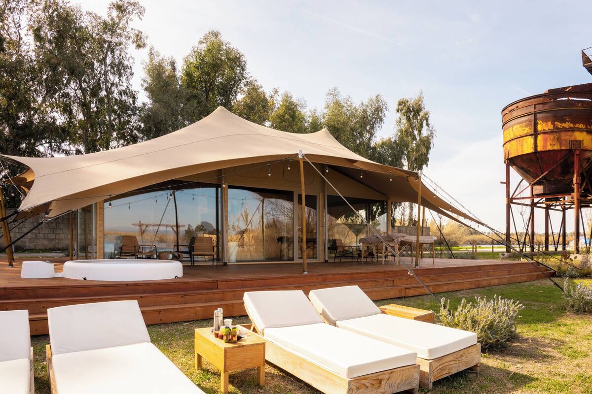 Ein moderner Außen-Loungesbereich mit Holzdeck, weißen Lounge-Sesseln und einer großen Markise.
