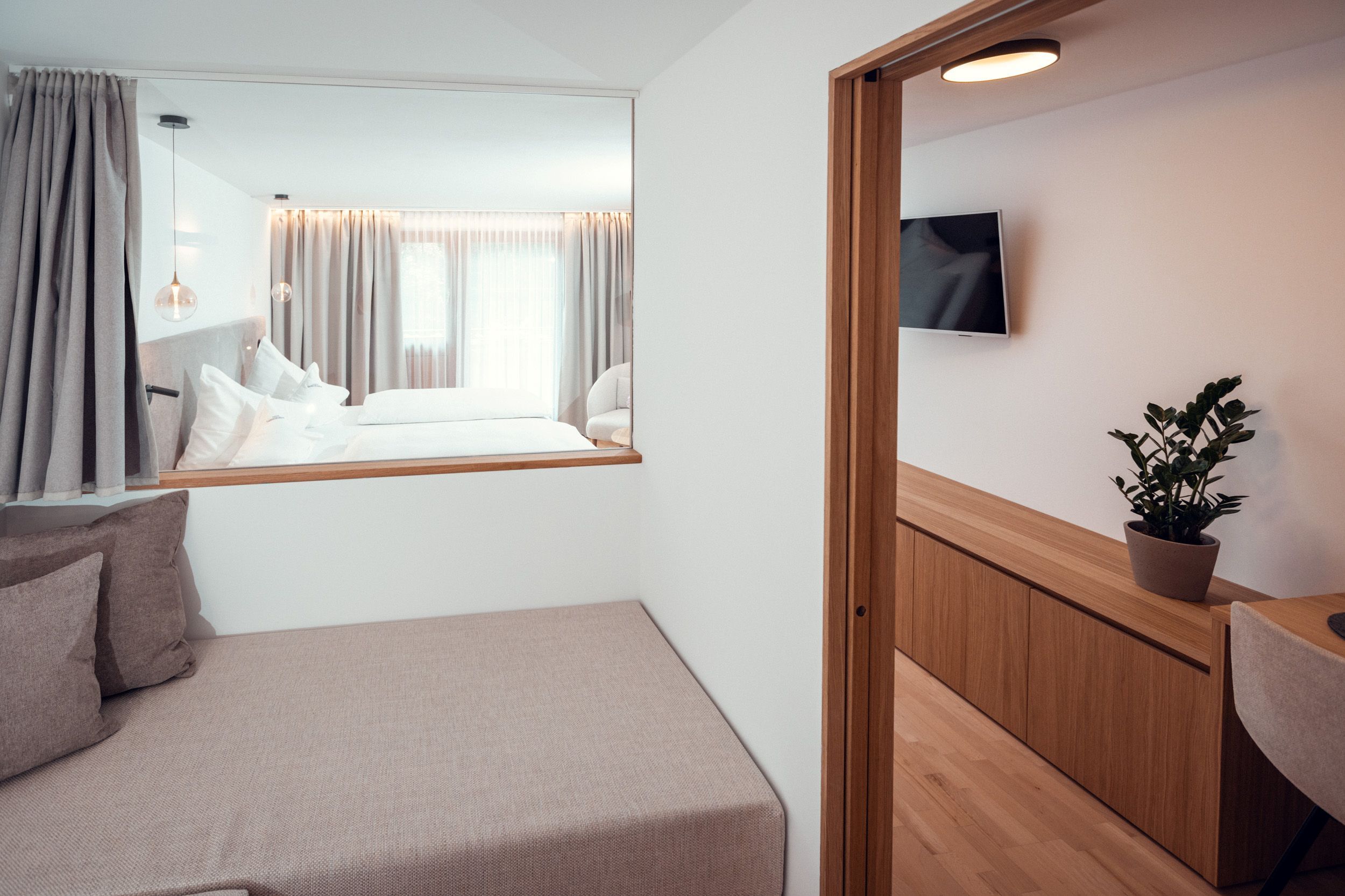 Een hotelkamer met een bed, een klein bureau, een bloempot en een televisie aan de muur.