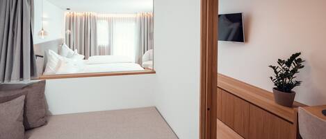 Een hotelkamer met een bed, een klein bureau, een bloempot en een televisie aan de muur.