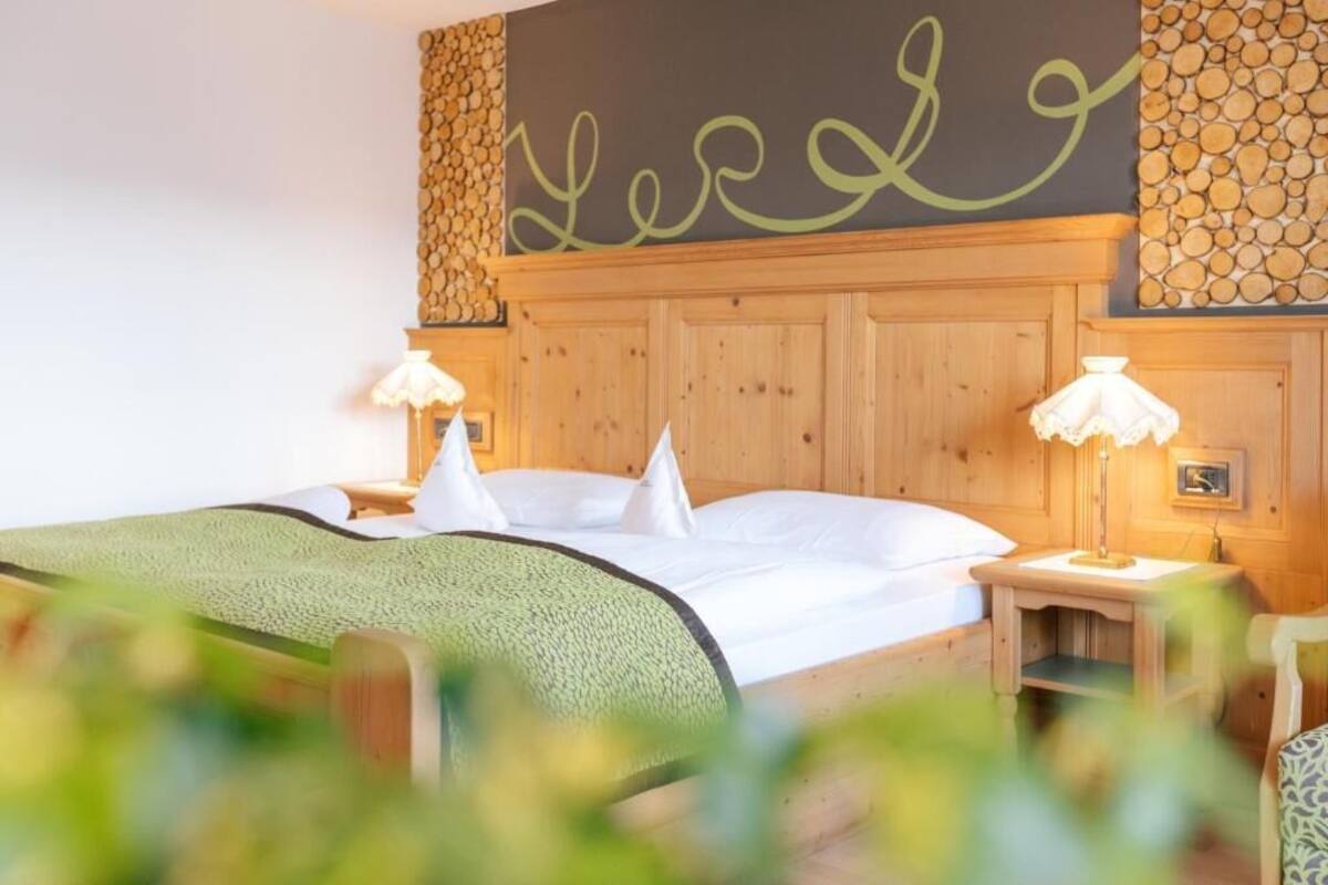 A neatly made bed with white linens and pillows, a wooden headboard, and two bedside lamps.
