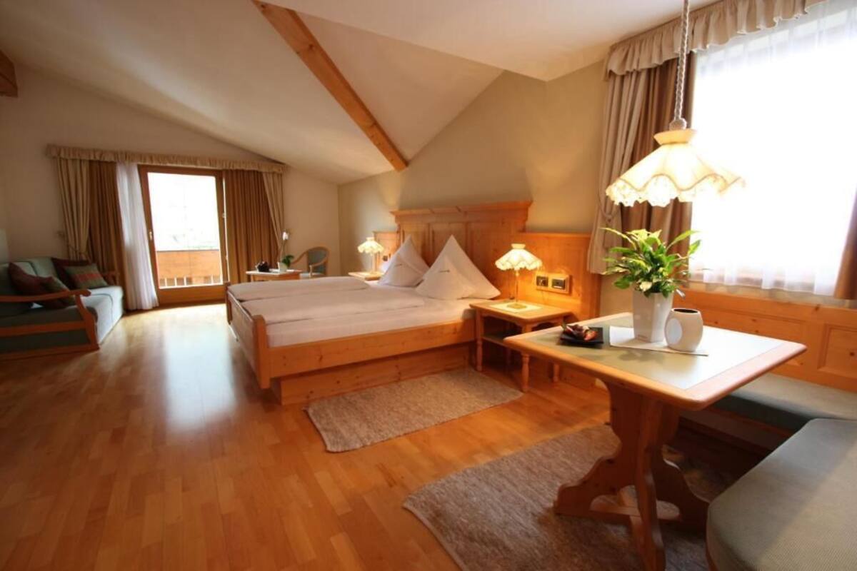 A cozy bedroom with a wooden bed, a desk, a chair, and a window with curtains.