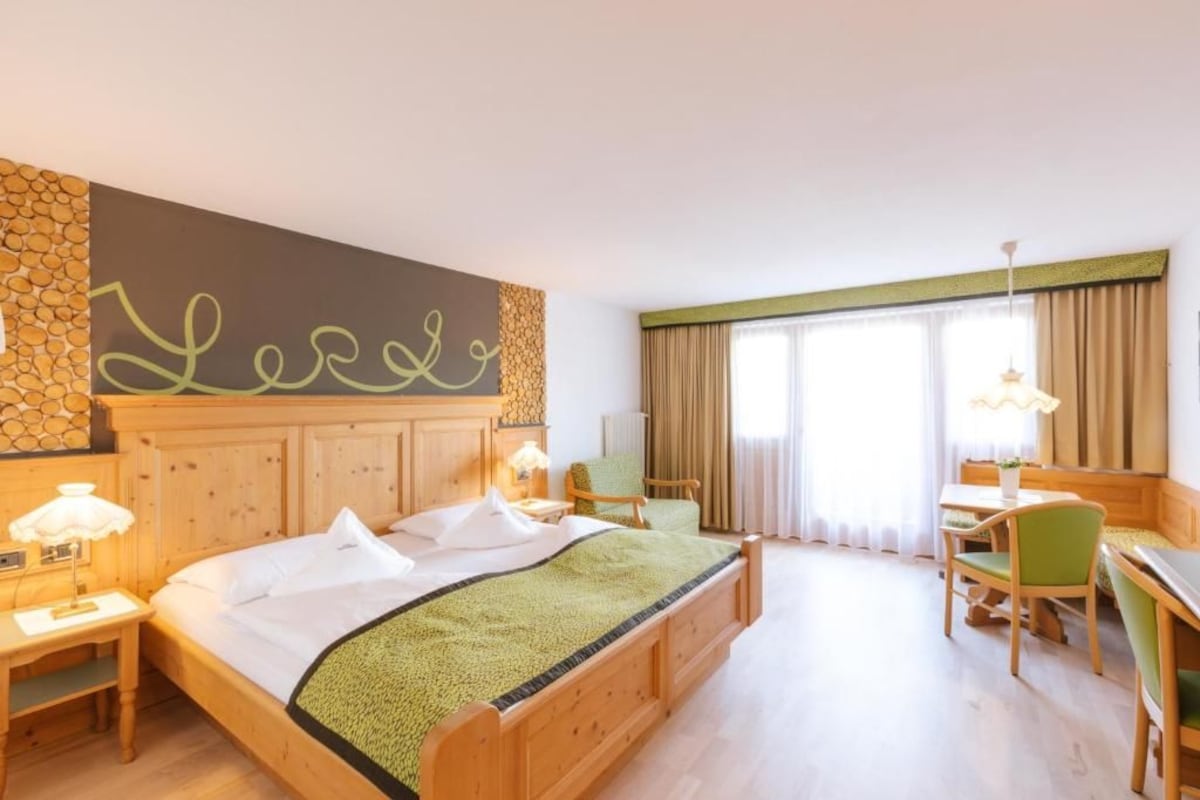 A hotel room with a bed, a desk, a chair, a lamp, and a wall with a decorative element.