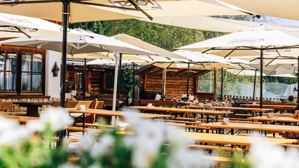 Een buitenterras met houten tafels en witte parasols.