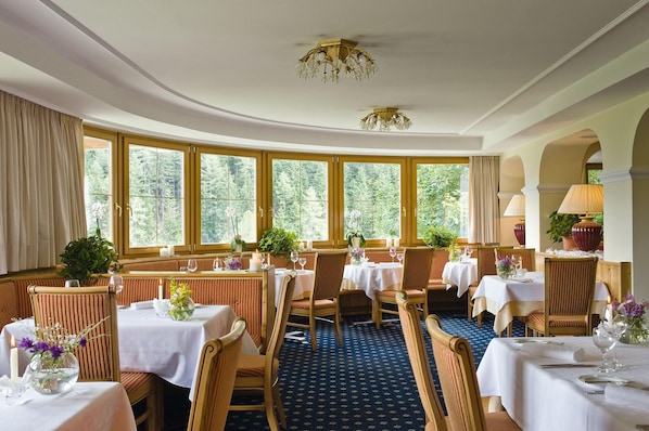 A restaurant with round tables, chairs, and large windows with curtains. - Ganischgerhof - Mountain Resort & Spa (Nova Ponente)