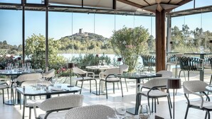 Un espace de restauration en plein air, avec des tables et des chaises, offrant une vue panoramique sur une colline et un plan d’eau.