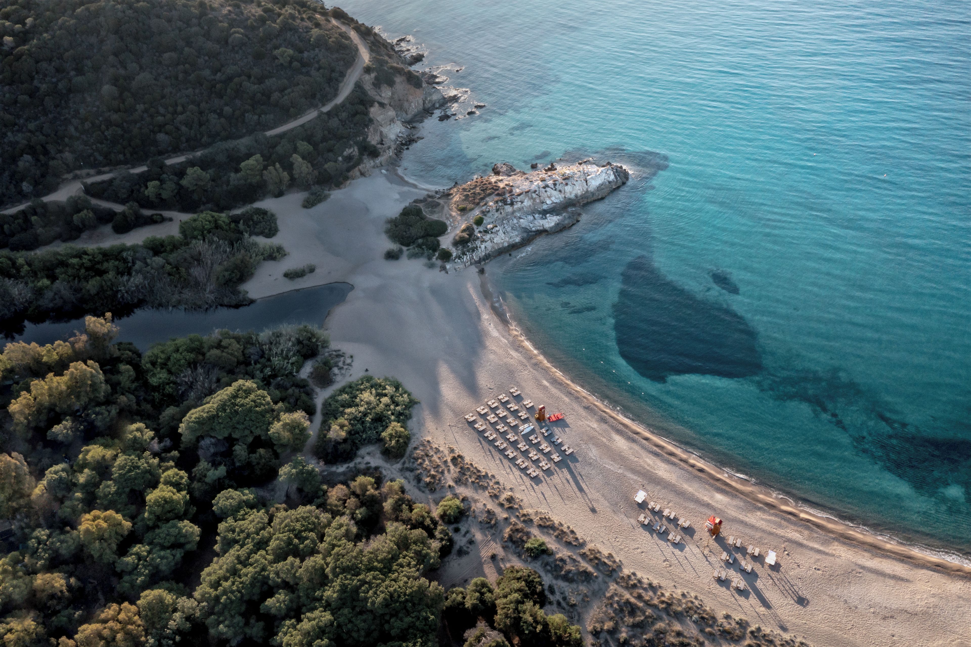 An aerial view of a coastal area with a beach, a rocky outcrop, and dense greenery.