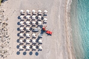 Vista aérea de una playa con hileras de sombrillas y sillas de playa, una torre de salvavidas y aguas azules cristalinas.