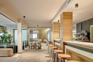 Un hall d’hôtel moderne doté d’un bar, d’espaces aménagés pour s’asseoir et offrant une vue sur l’extérieur.
