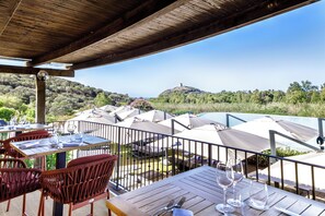 An outdoor dining area with tables and chairs, umbrellas, and a view of a hill with a tower. - Veridia Resort, a Member of Radisson Individuals (Domus de Maria)