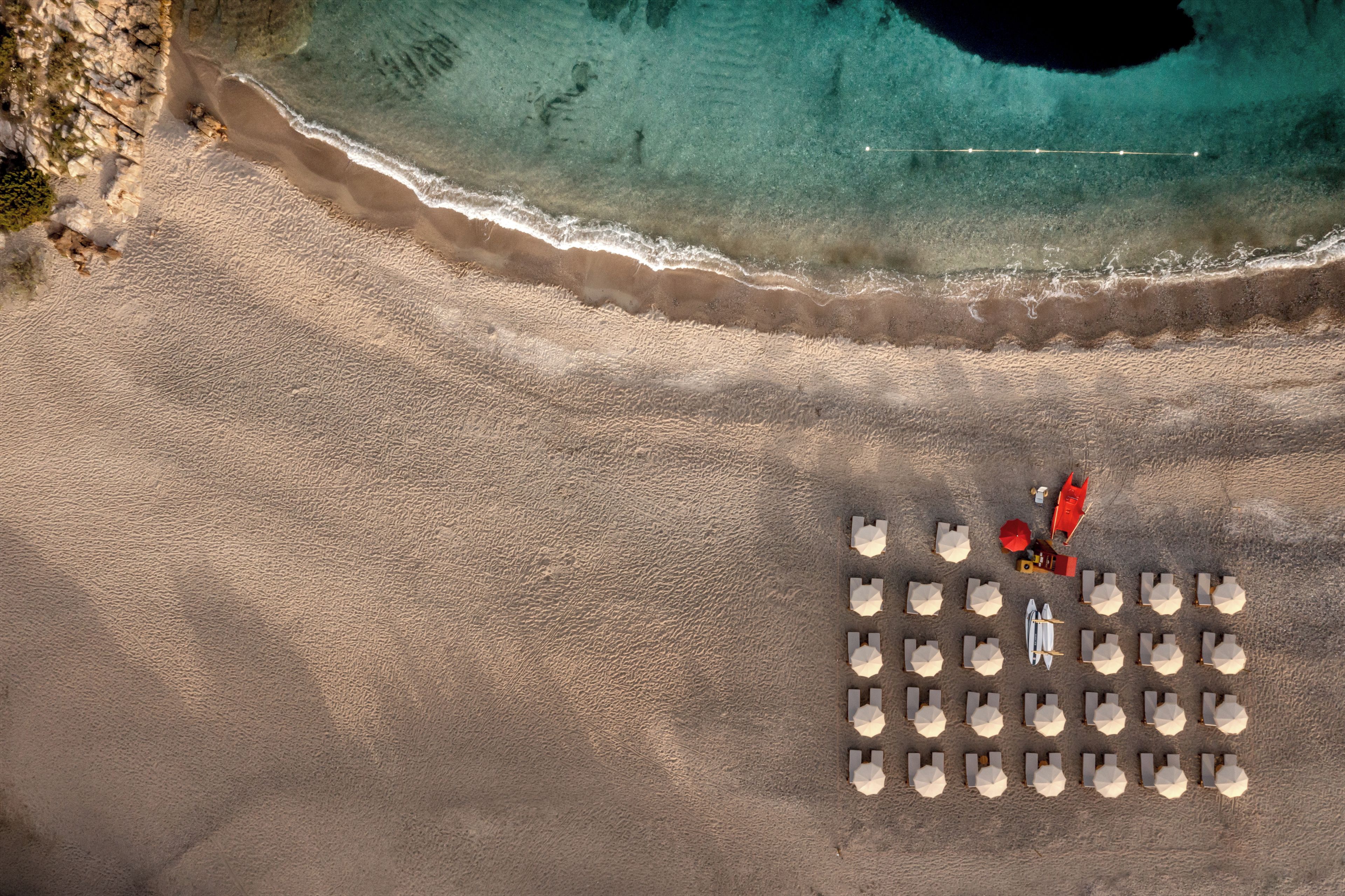 An aerial view of a beach with a row of umbrellas and a red lifeguard stand.