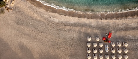 An aerial view of a beach with a row of umbrellas and a red lifeguard stand.