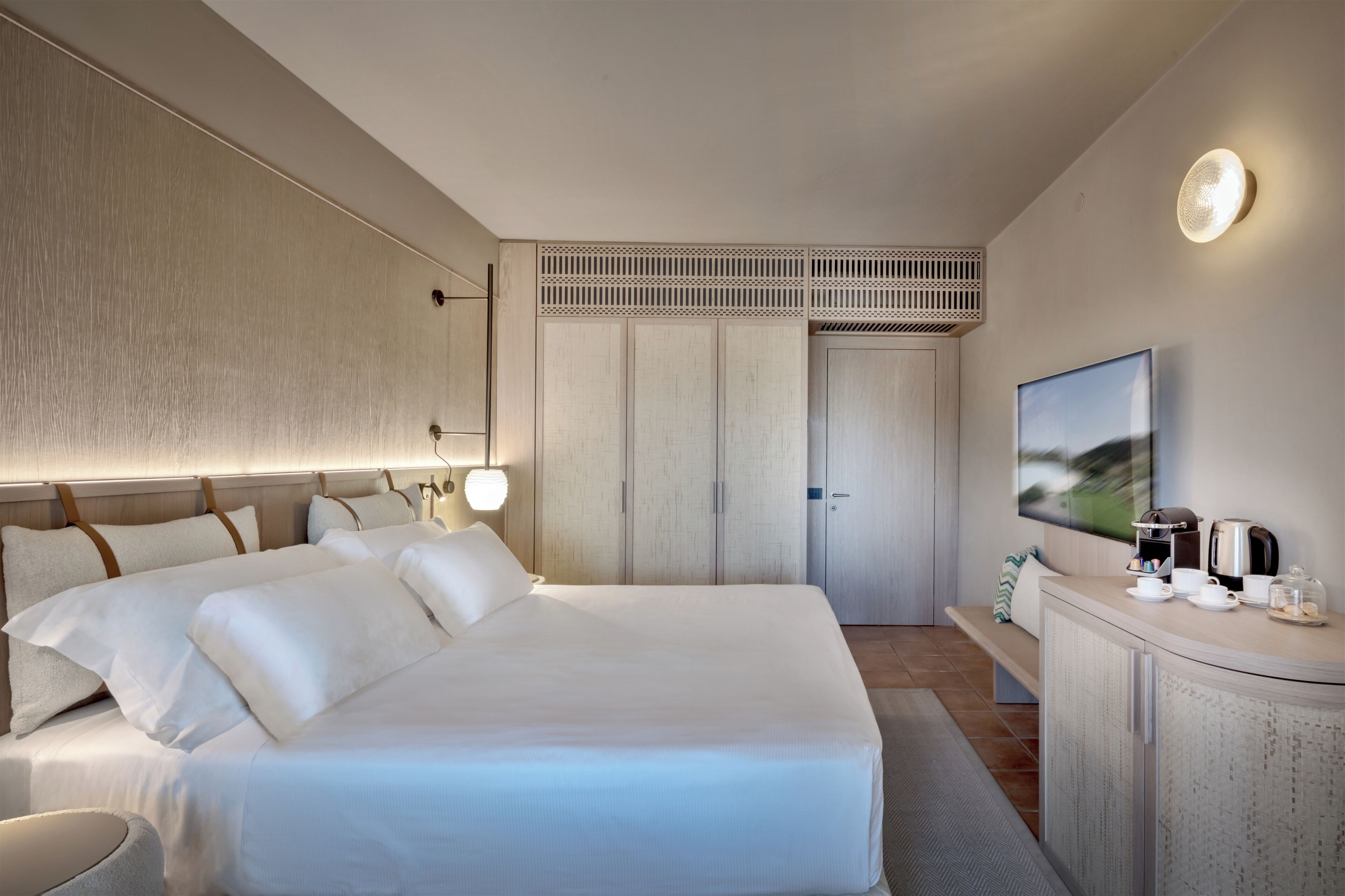 A modern hotel room with a large bed, a flat-screen TV, a coffee maker, and a wardrobe.