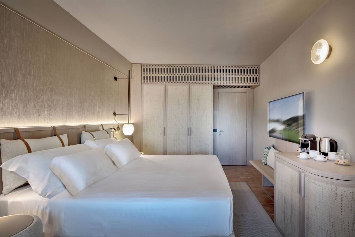 Quarto de hotel moderno com uma cama grande, uma TV de tela plana, uma cafeteira e um guarda-roupa.