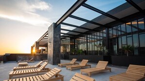 Een dakterras met houten ligbedden en een glazen gebouw op de achtergrond.