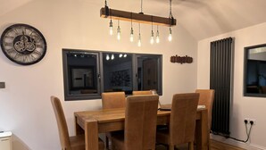 A dining area with a wooden table and chairs, a wall clock, and a modern pendant light fixture.