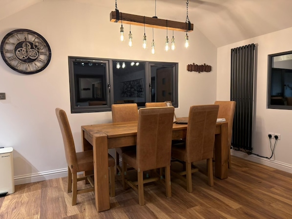 Un comedor con una mesa y sillas de madera, un reloj de pared y una lámpara colgante moderna.