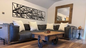 A modern living room with a sectional sofa, a wooden coffee table with wheels, and a large mirror on the wall.