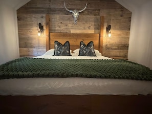 Un dormitorio con cabecera de madera, dos lámparas de pared y una calavera decorativa.