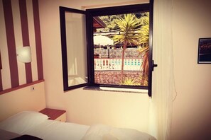 A bedroom with a bed, a window with a view of a pool and palm trees, and a wall-mounted light fixture. - Fonte Di Bagnaria Residence (Ricadi)