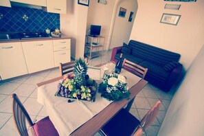 Un coin repas avec une table dressée pour deux personnes, une cuisine en arrière-plan et un canapé.