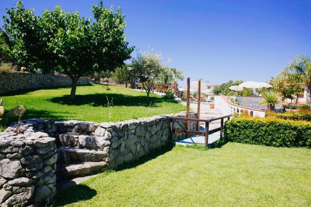 A stone wall, a wooden pergola, and a well-maintained lawn with a tree.
