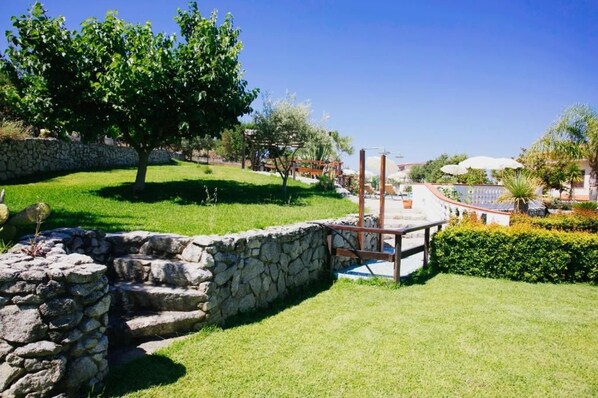 Un mur de pierres, une pergola en bois et une pelouse bien entretenue avec un arbre.