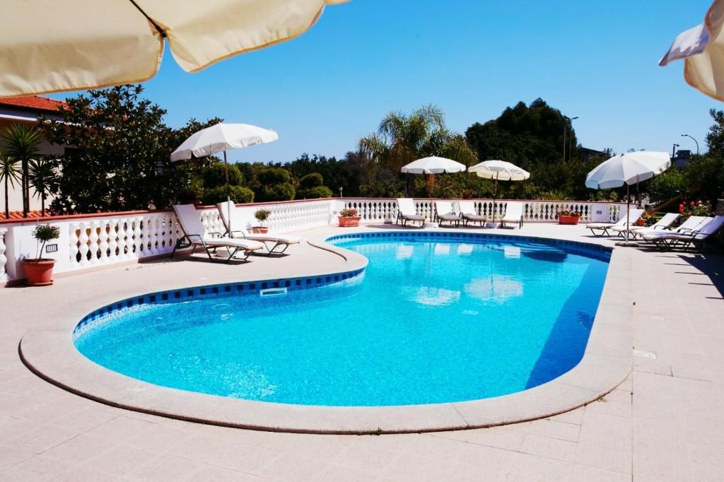 A swimming pool with lounge chairs and umbrellas, surrounded by a white fence and greenery.