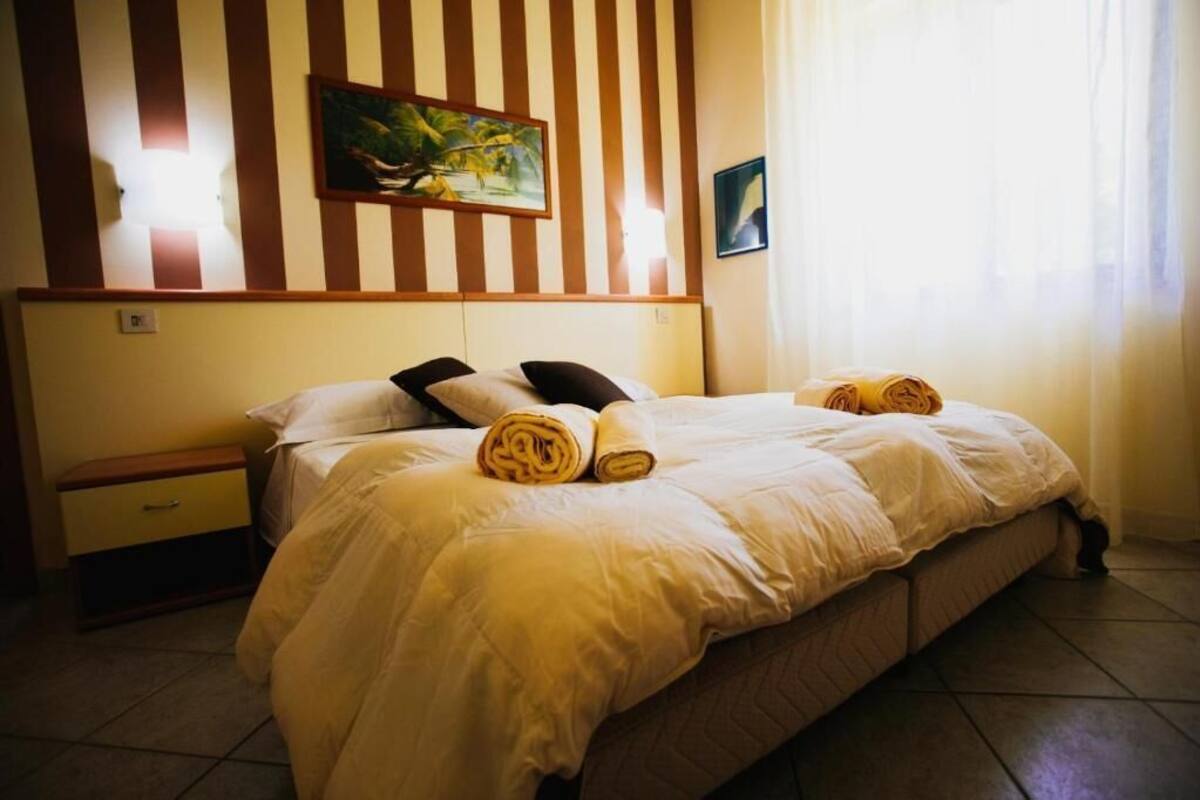 A hotel room with a bed, a nightstand, a painting, and a window with curtains.