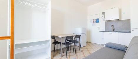 A compact room with a bed, a kitchenette, a dining area, and a wardrobe.